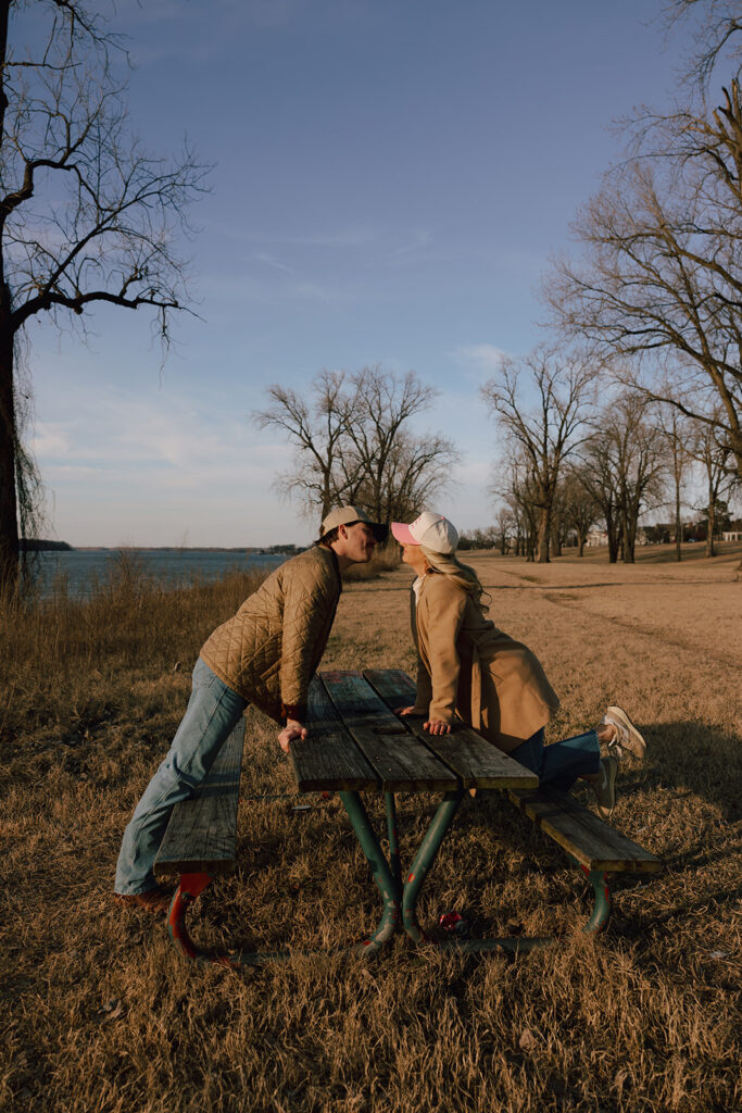 Couple leaning over a picnic table to kiss at the park in Memphis, TN for engagement photos